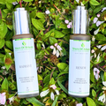 Two 1 oz Tears of Beauty serums, Radiant (Hyaluronic Acid) and Renew (Vitamin C Retinol), on green leaves with pink flowers.